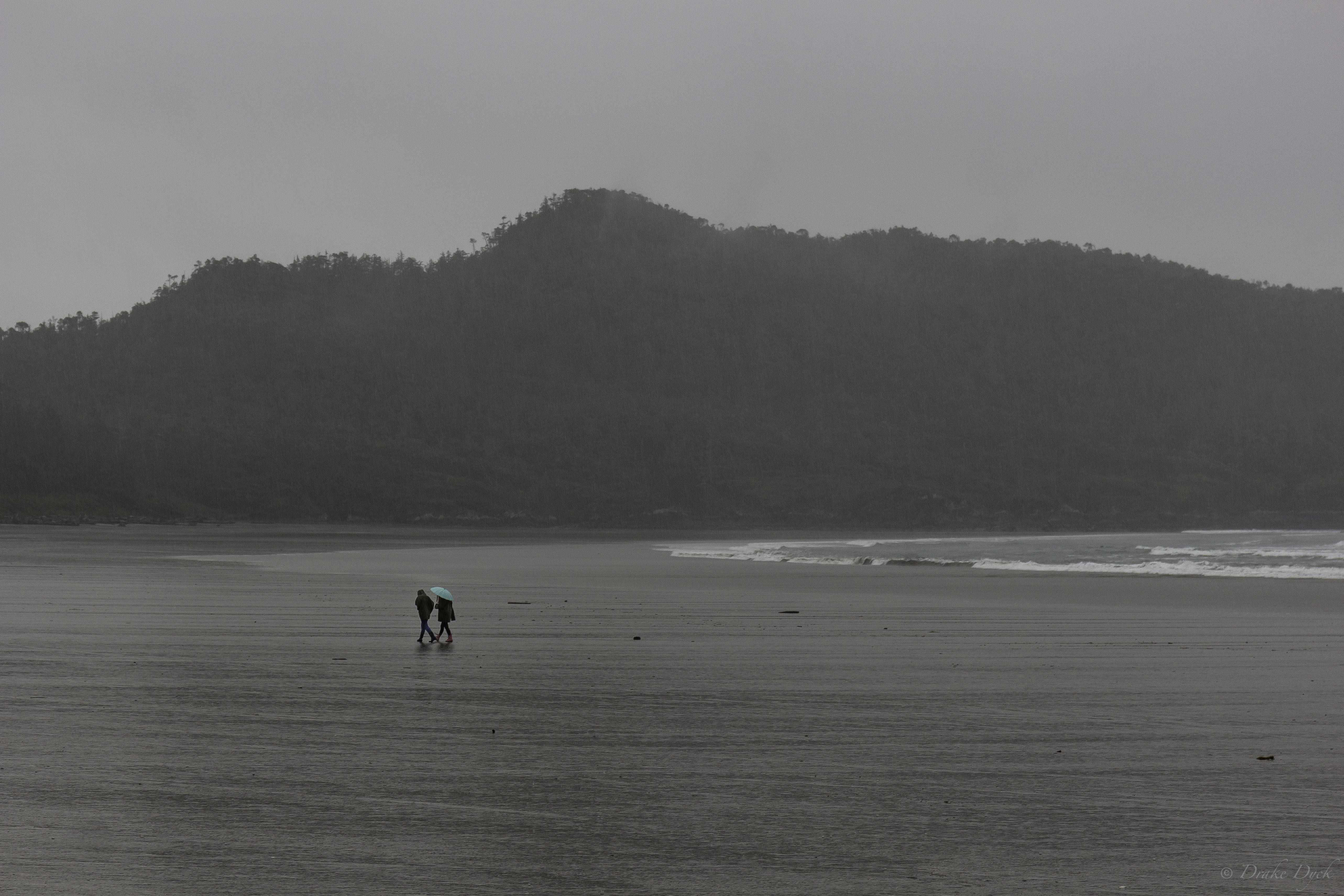 a couple with a colourful umbrella walk in a downpour on the beach