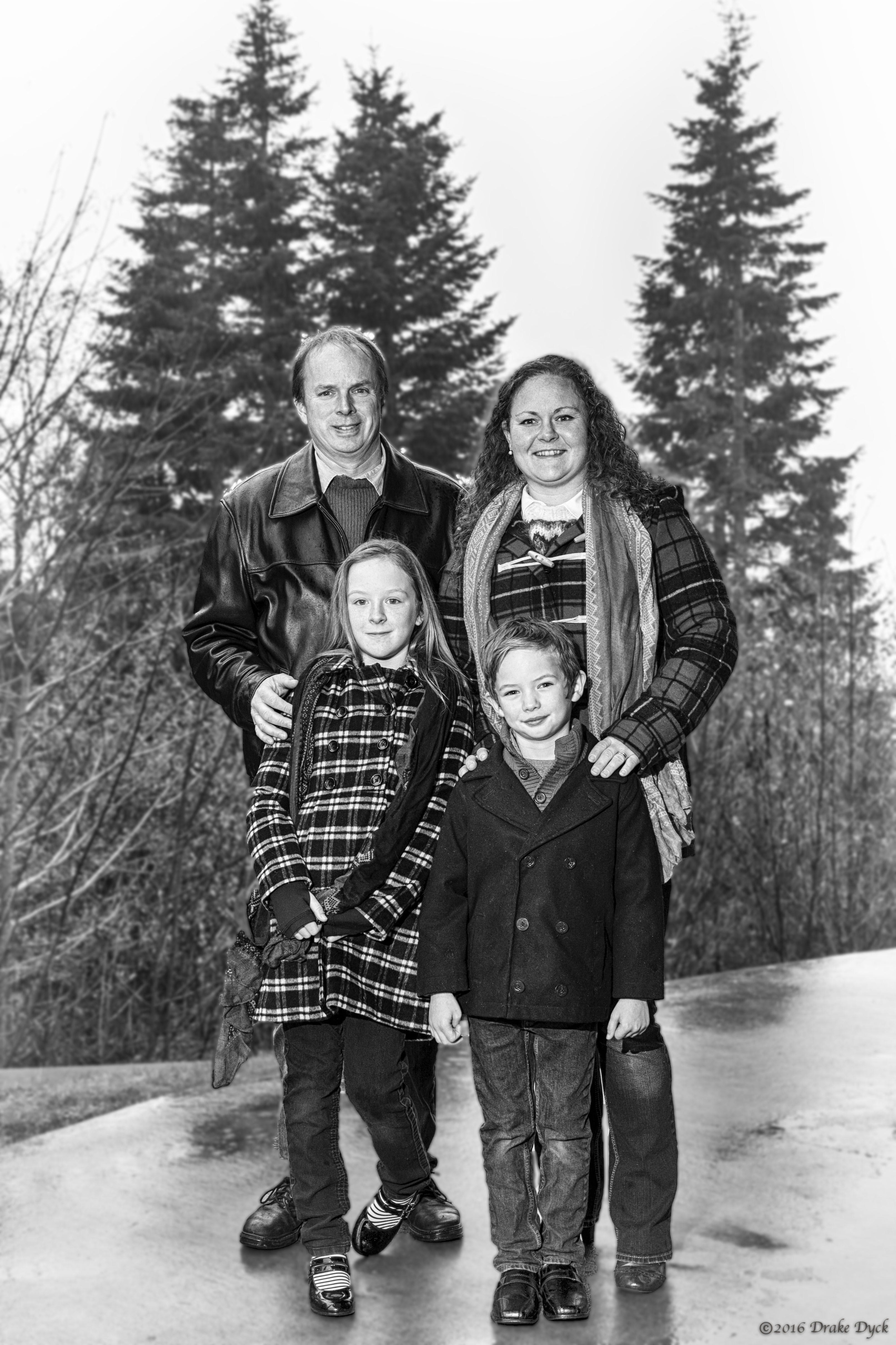 family of four in black and white in front of trees