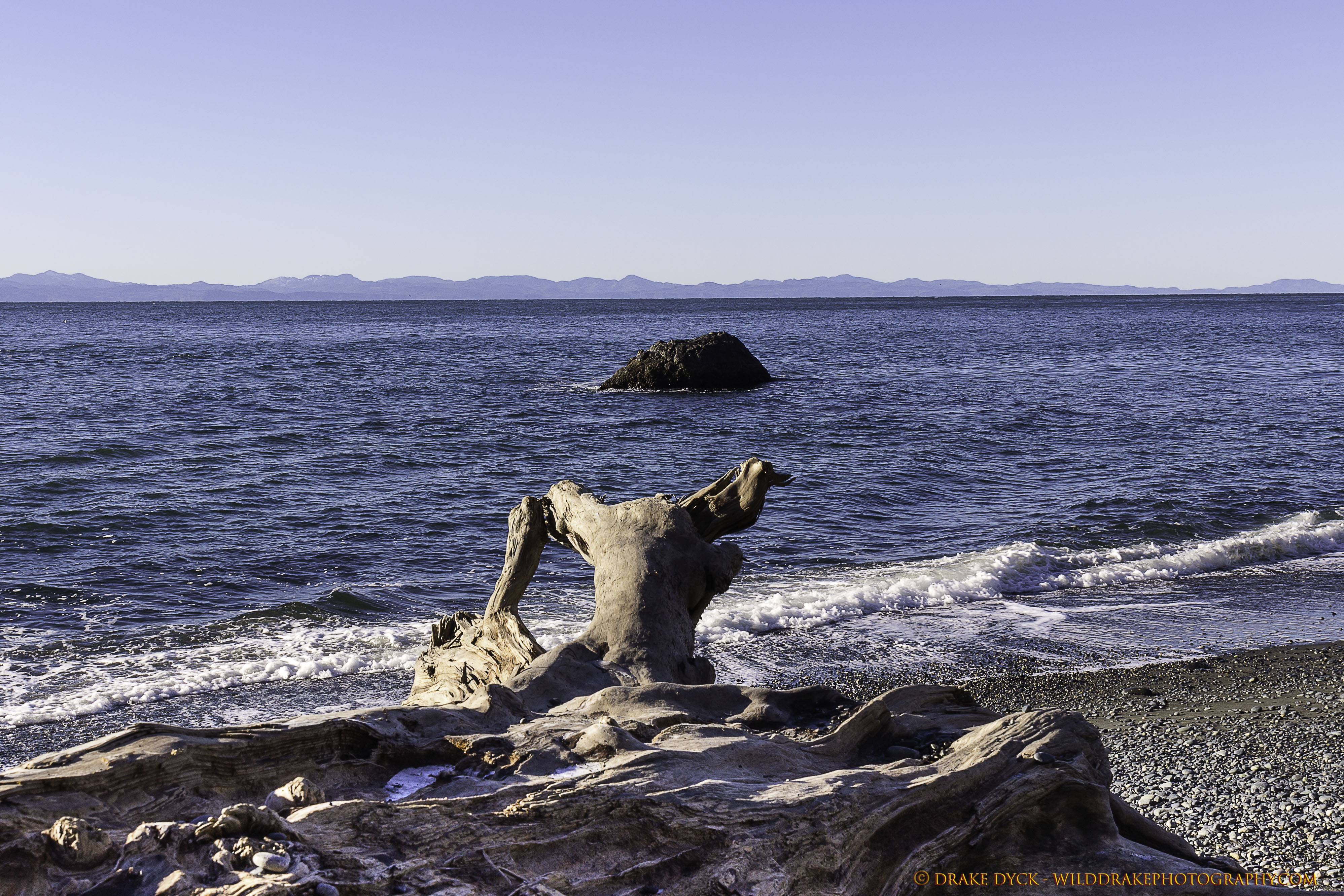 Log on beach overlooking rock and Olympic Peninsula