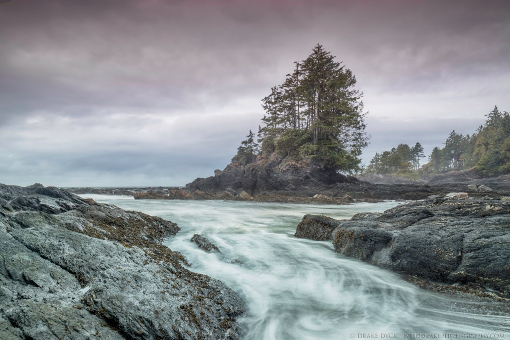waves crash on the beach then return to the ocean past a small islet