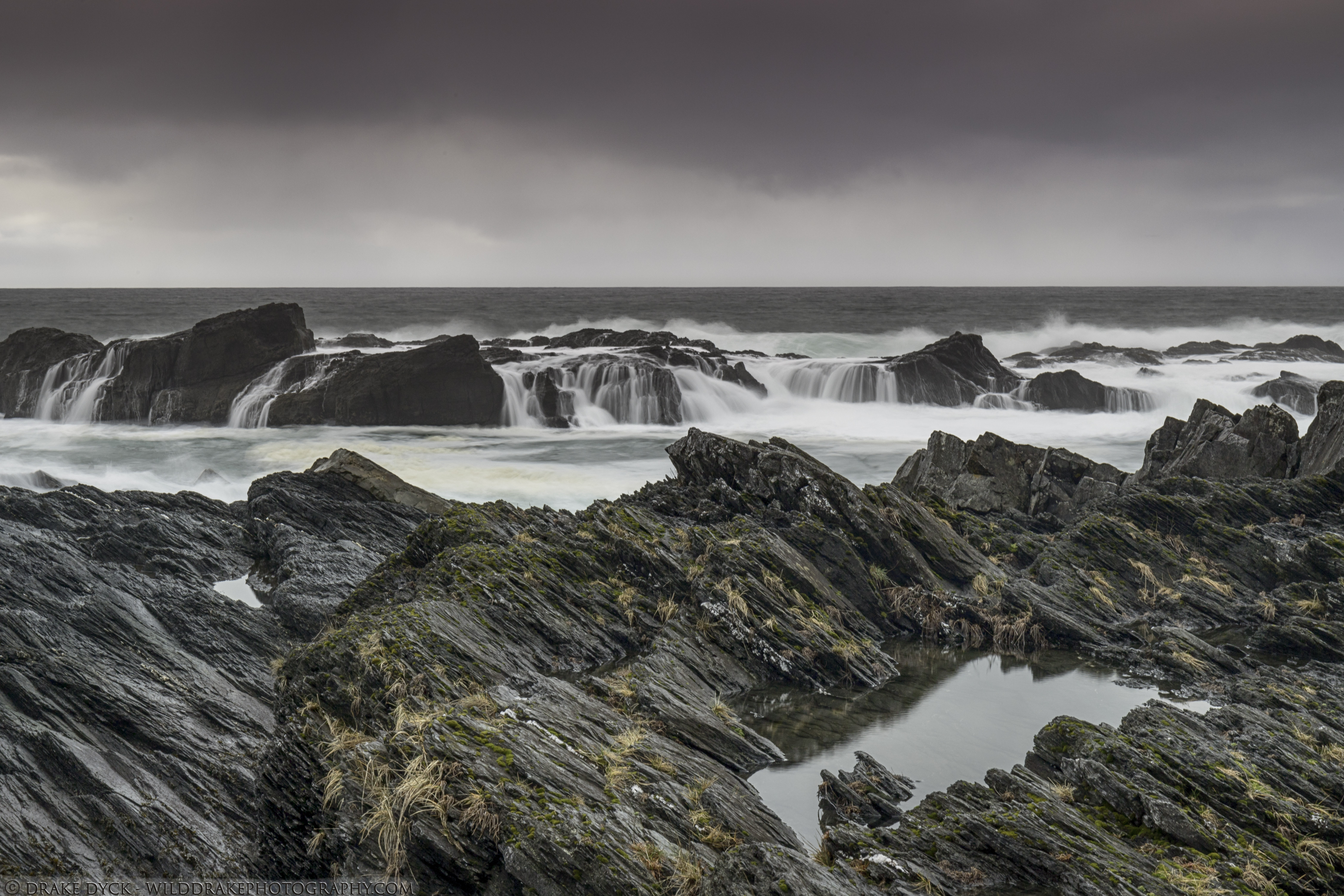 angled layers of rock jut out from a turbulent sea
